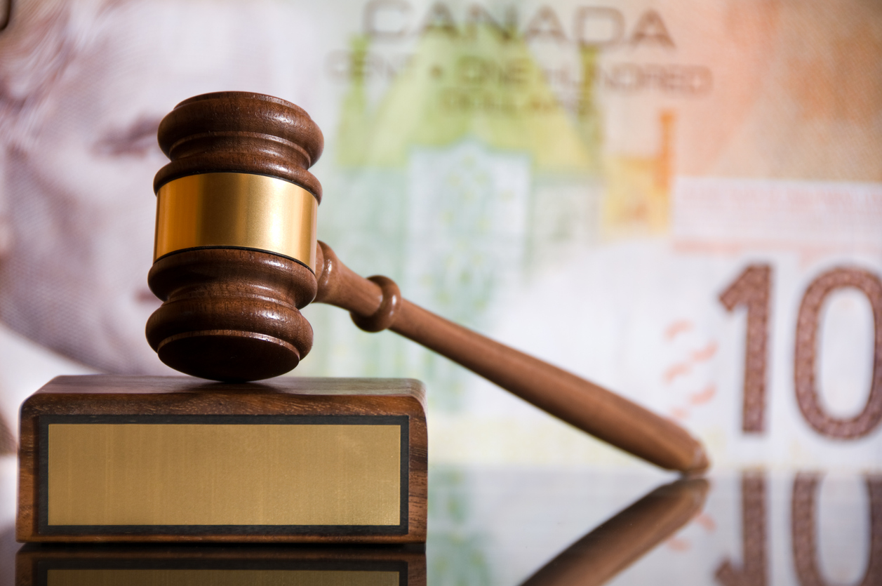 A judge's gavel is seen in front of an out-of-focus canadian hundred dollar bill. Three Ontario Online Casinos Fined for Offering Uncertified Slots